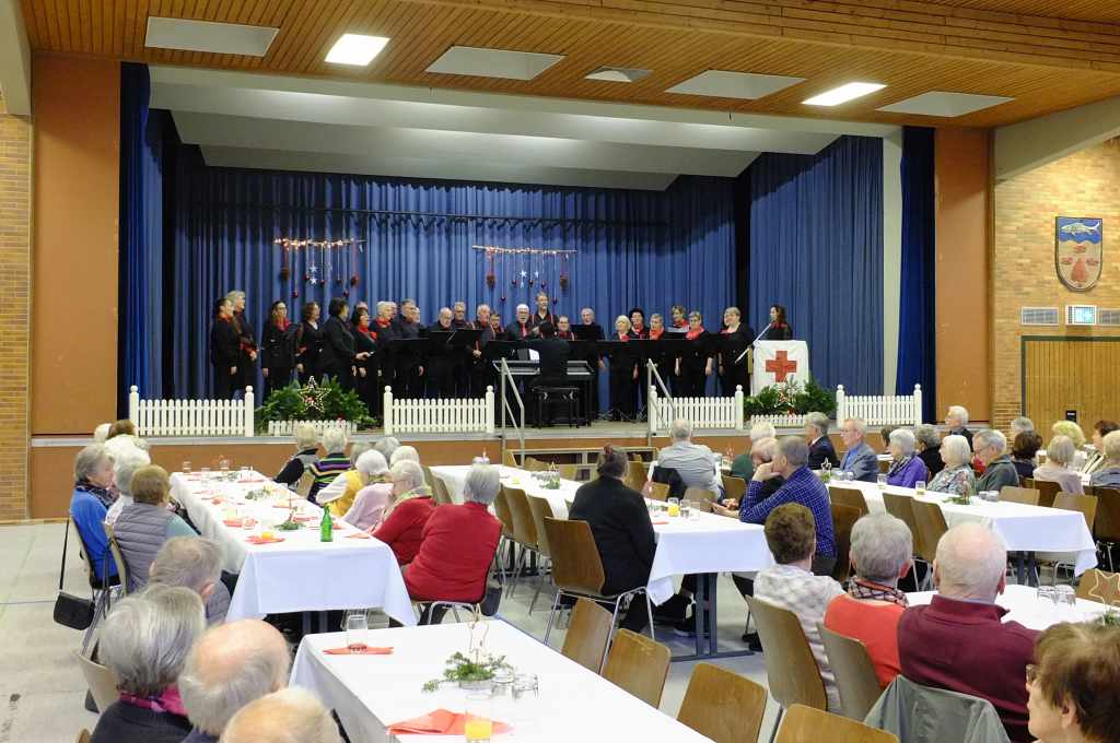 Das Foto zeigt die Bühne der Steinacher Turn- und Festhalle, auf der der Gesangverein "Unser Chor" zu sehen ist. Im Publikum sitzen Senioren.